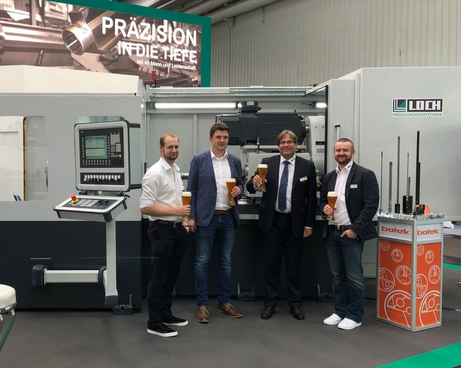 Eine Tiefbohrmaschine der Loch Präzisions Bohrtechnik auf einer Messe, davor vier Mitarbeiter